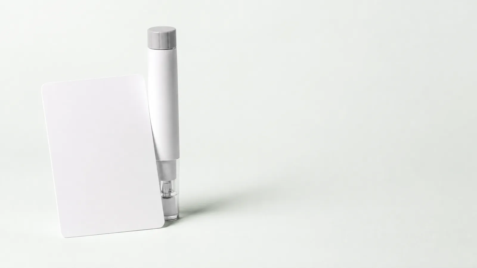 Studio still life: a blank card leaning on an unbranded pen injector
