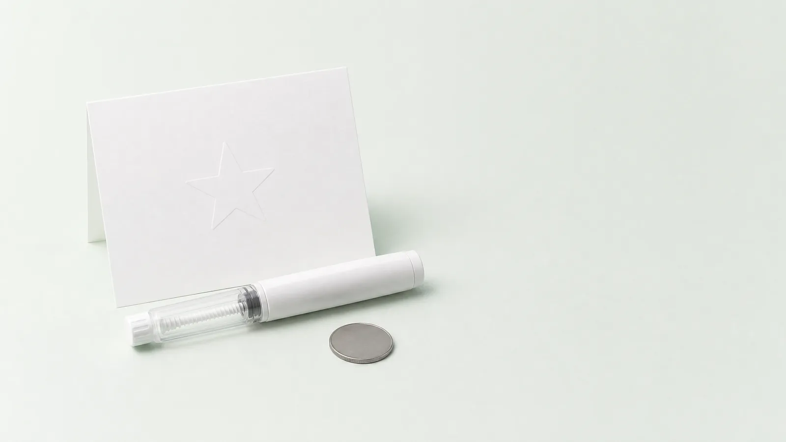 Studio still life: a blank card, an unbranded pen injector and a single coin